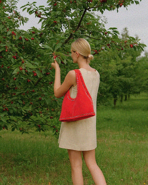 Woman in a dress with a red bag picking cherries in an orchard
